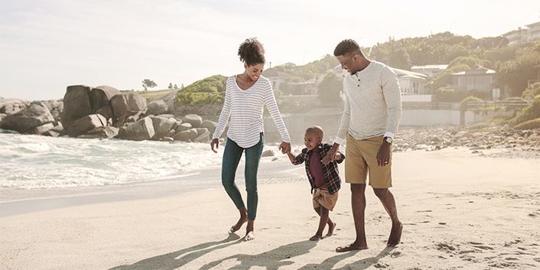 Two parents walk on a beach, each holding a hand of their young child