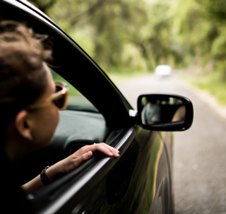 Person slightly leans out the passenger window of a car on a wooded road
